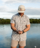 Person wearing a camouflage-patterned button-down shirt with a visible brand logo on a white background