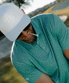 Man wearing a teal golf club and golf ball  dot polo shirt on a white background