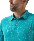 Man wearing a teal golf club and golf ball  dot polo shirt on a white background