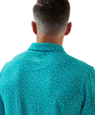 Man wearing a teal golf club and golf ball  dot polo shirt on a white background