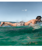 Man swimming in the ocean wearing camo swim shorts on a clear blue sky above
