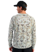 Man wearing a camouflage long-sleeve shirt with a HUK brand logo on the back, against a white background