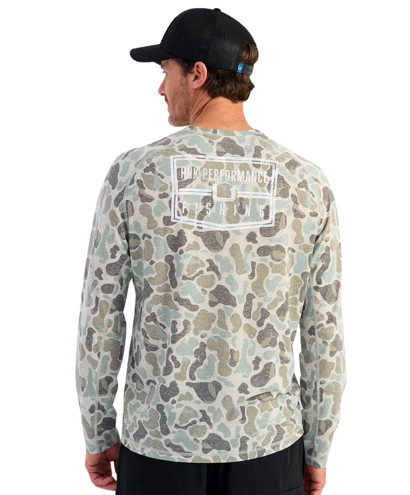 Man wearing a camouflage long-sleeve shirt with a HUK brand logo on the back, against a white background