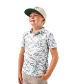 Child wearing a CAMO patterned polo shirt and cap on a white background