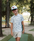 Child wearing a CAMO patterned polo shirt and cap on a white background
