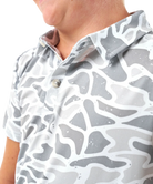 Child wearing a CAMO patterned polo shirt and cap on a white background