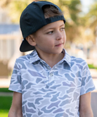 Child wearing a CAMO patterned polo shirt and cap on a white background