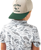 Child wearing a CAMO patterned polo shirt and cap on a white background