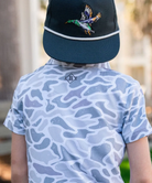 Child wearing a CAMO patterned polo shirt and cap on a white background